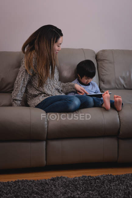 Vista frontal da mãe e do filho asiáticos usando tablet digital enquanto estão sentados no sofá em casa — Fotografia de Stock