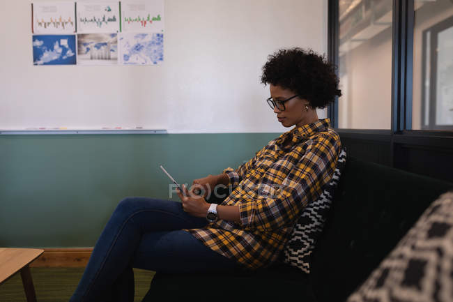 Seitenansicht der schönen gemischtrassigen Geschäftsfrau mit digitalem Tablet, die im modernen Büro sitzt — Stockfoto