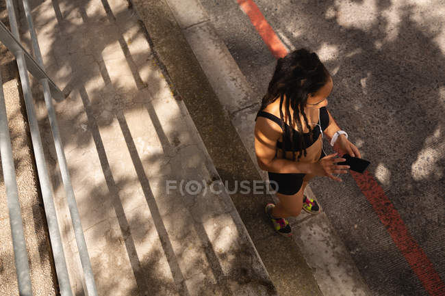 Vista de alto ângulo da jovem mulher de raça mista usando telefone celular na rua da cidade — Fotografia de Stock
