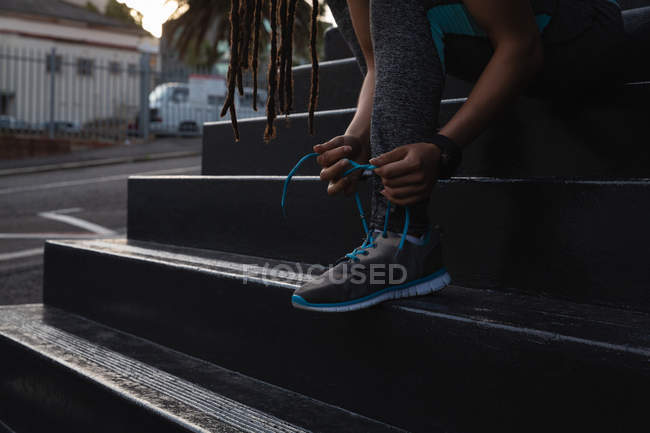 Sección baja de mujer en forma atándose los cordones de los zapatos en las escaleras de la ciudad - foto de stock