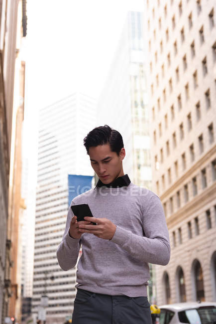 Vista de ángulo bajo del hombre asiático usando el teléfono móvil mientras está de pie en la calle - foto de stock