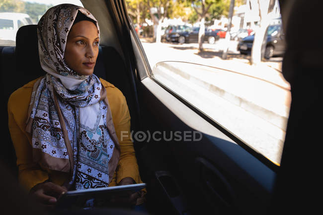 Vorderansicht der schönen Mischlingshündin, die durch das Fenster schaut und während der Fahrt im Taxi ein digitales Tablet in der Hand hält — Stockfoto