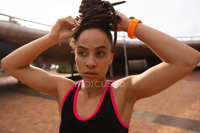 Portrait of thoughtful Mixed race young woman tying her updo in the city — Stock Photo
