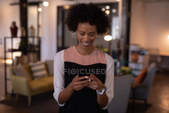 Вид спереду щасливої молодої бізнес-леді змішаної раси, що використовує мобільний телефон в сучасному офісі — стокове фото