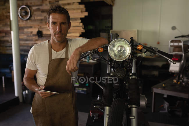Front view of Caucasian bike mechanic standing in garage while holding digital tablet — Stock Photo