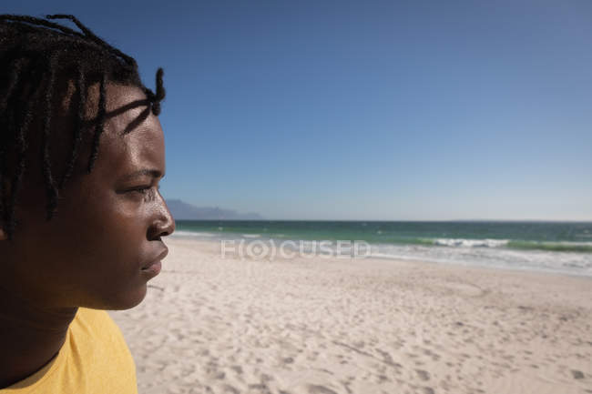 Перегляд профілю вдумливого молодого афроамериканського людини, стоячи на пляжі в сонячний день — стокове фото