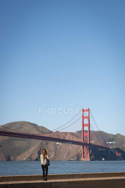Vue arrière de la femme marchant du mur assis près du pont de porte d'or — Photo de stock