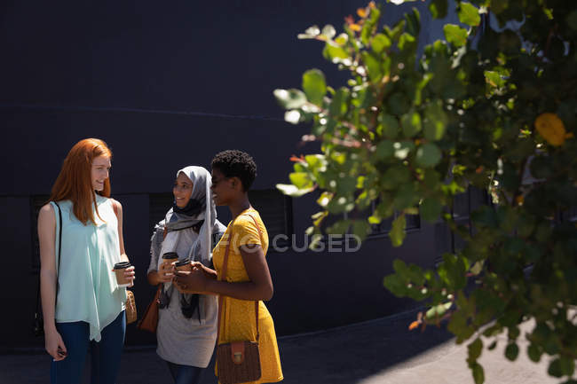Vista frontale di giovani amiche di razza mista che interagiscono tra loro nella strada della città nella giornata di sole — Foto stock