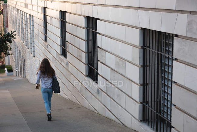 Вид ззаду жінки, що йде на тротуарі в місті — стокове фото