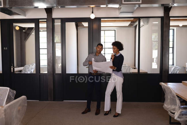 Вид спереду молодих бізнесменів змішаної раси, які обговорюють один одного і дивляться на план в новому офісі — стокове фото