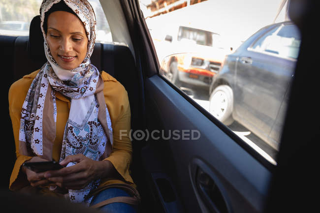 Frontansicht einer Frau, die lächelt und ihr Handy benutzt, während sie an einem sonnigen Tag im Auto unterwegs ist — Stockfoto