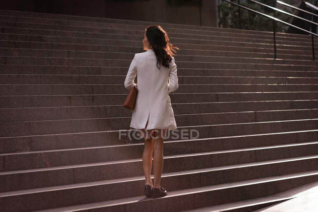Задумчивая азиатка, стоящая у лестницы в солнечный день — стоковое фото