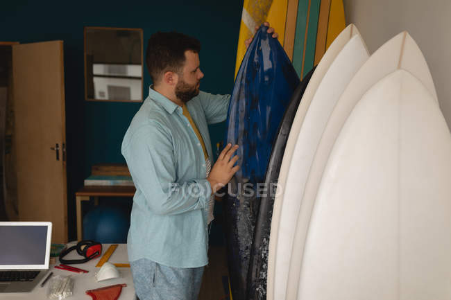 Vista lateral del hombre caucásico revisando y organizando tablas de surf en un taller - foto de stock