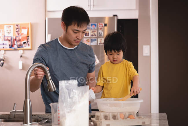 Vue de face du père et du fils asiatiques mélangeant la pâte dans la cuisine à la maison — Photo de stock