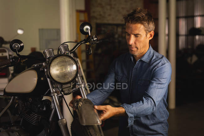 Vista frontal de la bicicleta masculina caucásica mecánico reparación de neumáticos de moto en el garaje - foto de stock