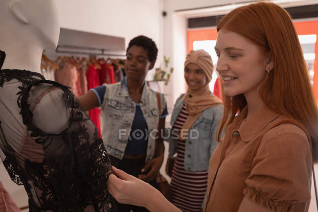 Side view of mixed race happy female friends choosing dress in boutique — Stock Photo