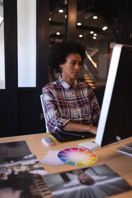 Вид спереди красивой женщины-графического дизайнера смешанной расы, работающей за компьютером в офисе с картинками на переднем плане — стоковое фото