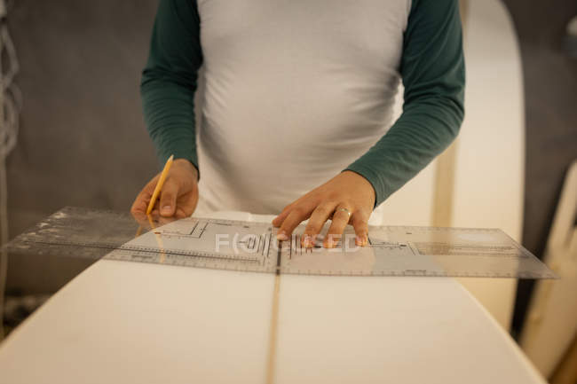 Section médiane de l'homme mesurant avec règle et crayon une planche de surf en atelier — Photo de stock