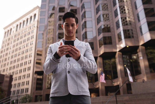 Vista basso angolo di bello asiatico uomo utilizzando il telefono cellulare mentre in piedi sulle scale — Foto stock