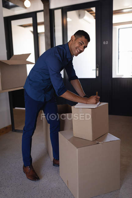 Portrait of young mixed-race businessman writing on diary at creative office. He is smiling and looking at camera — Stock Photo