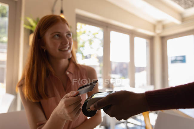 Vue latérale de belle jeune femme caucasienne effectuant le paiement par carte de crédit dans un café — Photo de stock