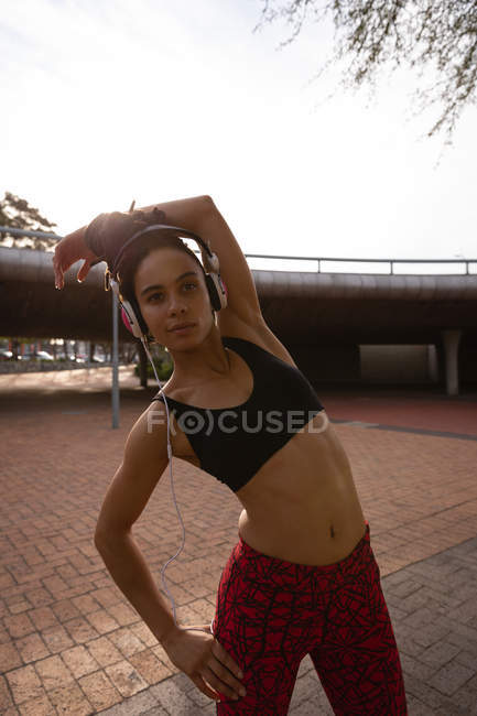 Vista frontale della giovane donna di razza mista che ascolta musica sulle cuffie mentre si esercita in città — Foto stock