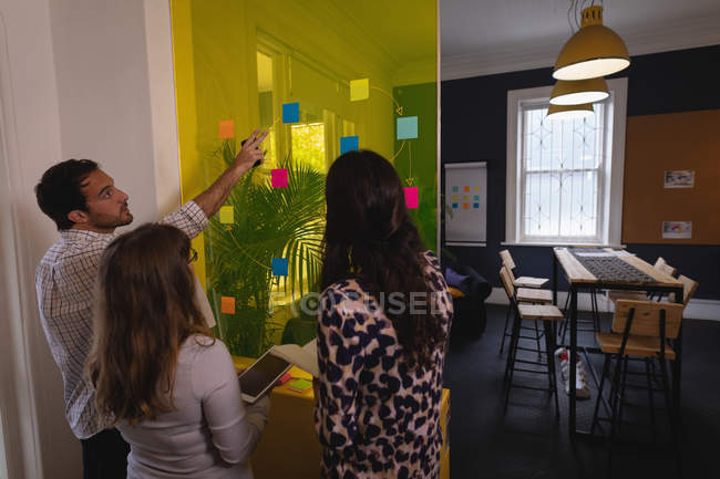 Visão traseira do atencioso Diversas pessoas de negócios discutindo sobre notas pegajosas na parede de vidro no escritório — Fotografia de Stock