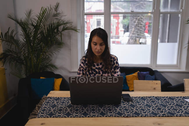 Вид спереду красива змішаної раси жінка-виконавця, що працює на ноутбуці за столом в офісі — стокове фото