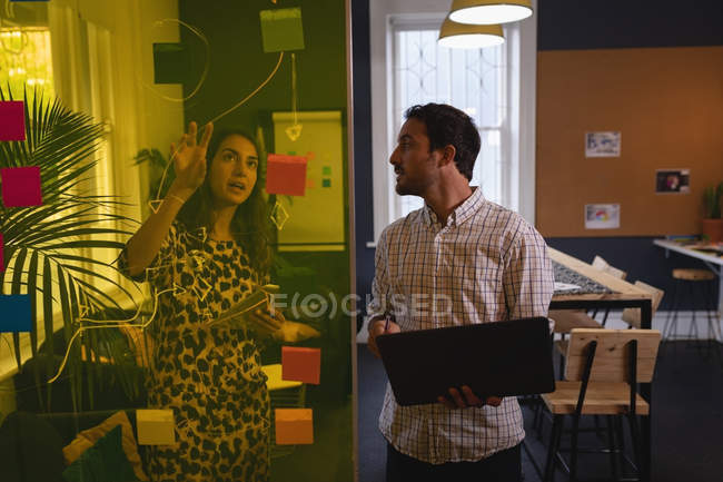 Вид спереду Різноманітні чоловічі та жіночі керівники обговорюють липкі ноти на скляній стіні в офісі — стокове фото
