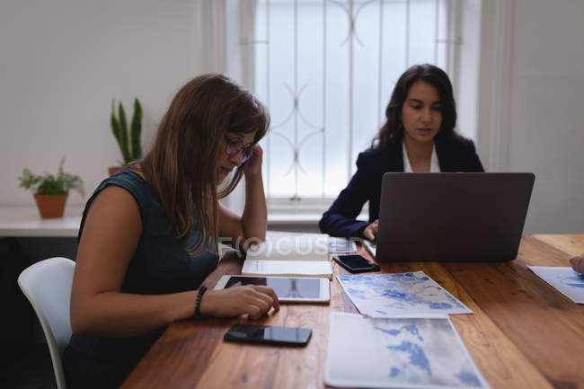 Вид сбоку на разнообразных предпринимательниц, работающих над ноутбуком и цифровым планшетом за столом в офисе — стоковое фото