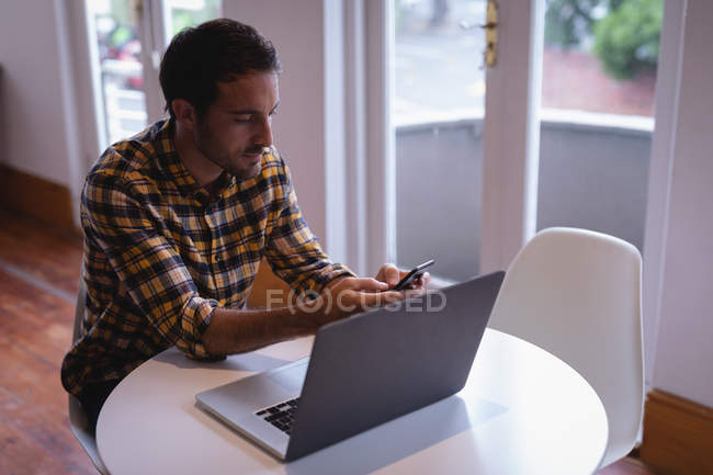 High angle view of Caucasian male executive using mobile phone while working on laptop in the office — Stock Photo
