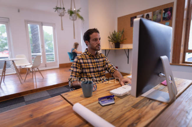 Вид сбоку на внимательного кавказца, работающего за компьютером за столом в офисе — стоковое фото