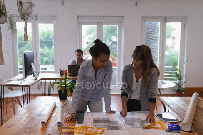 Frontansicht schöner unterschiedlicher Geschäftsfrauen, die im Büro über Baupläne diskutieren — Stockfoto