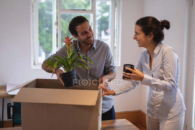 Vista frontal del hombre de negocios caucásico y la mujer de negocios de raza mixta que interactúan entre sí mientras empacan cajas de cartón en la oficina - foto de stock