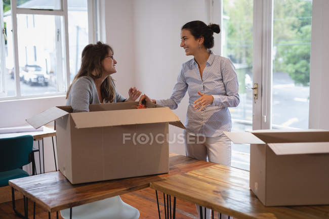 Вид сбоку на красивых бизнесвумен, упаковывающих картонные коробки в офисе — стоковое фото