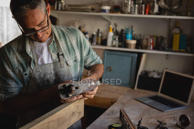 Vorderansicht des aufmerksamen reifen kaukasischen Zimmermanns mit glattem Hobel auf Holzplanke in der Werkstatt — Stockfoto