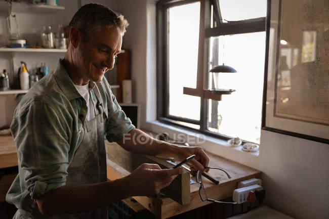 Вид сбоку на счастливого взрослого кавказского плотника с помощью мобильного телефона в мастерской — стоковое фото