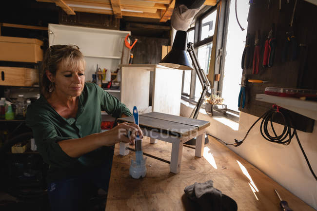 Vista frontal del atento taburete de pintura de carpintero femenino caucásico en el taller - foto de stock