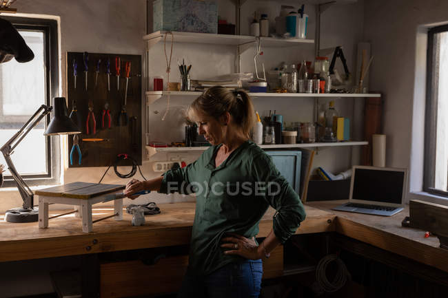 Vue latérale du tabouret de peinture de charpentier féminin caucasien attentif dans l'atelier — Photo de stock
