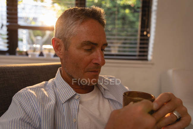 Front view of thoughtful mature Caucasian man holding coffee in living room at home — Stock Photo