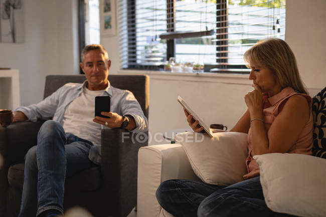 Seitenansicht eines reifen kaukasischen Paares mit digitalem Tablet und Mobiltelefon im heimischen Wohnzimmer — Stockfoto