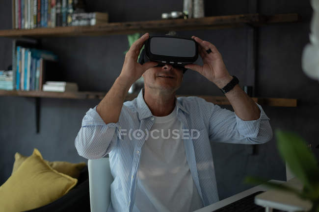 Вид з зрілої кавказької людини за допомогою гарнітури віртуальної реальності у вітальні вдома — стокове фото