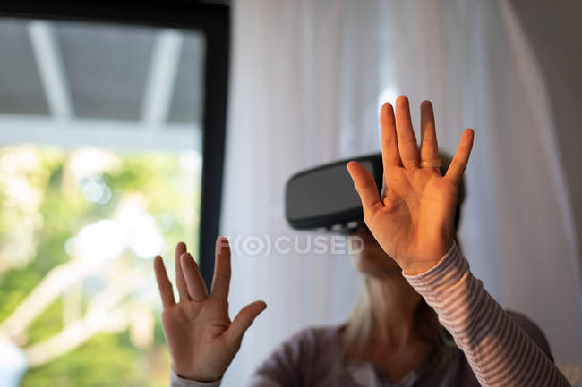 Вид зрелой кавказской женщины с гарнитурой виртуальной реальности в гостиной дома — стоковое фото