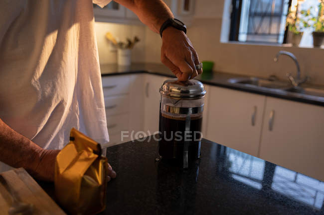 Seção média do homem preparando café na cozinha em casa ao nascer do sol — Fotografia de Stock