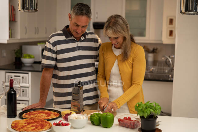 Vue de face d'une femme blanche mature heureuse tranchant des champignons et préparant une pizza dans la cuisine à la maison — Photo de stock