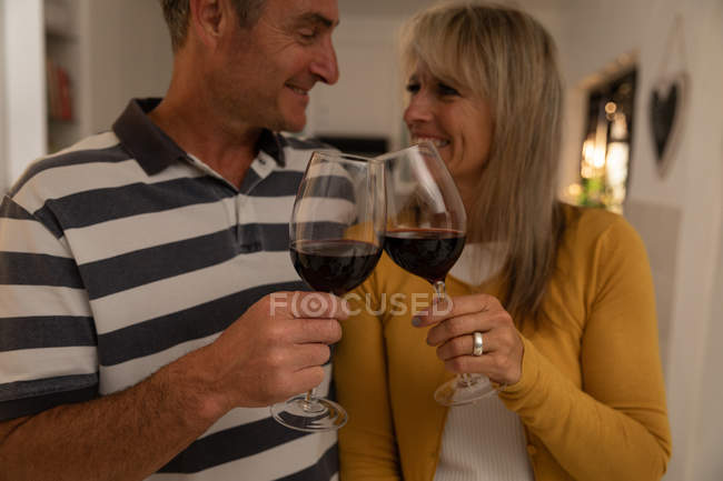 Vorderseite des glücklichen reifen kaukasischen Paares, das in der Küche Weingläser anstößt, während es sich zu Hause anschaut — Stockfoto