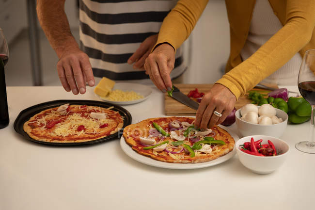 Средняя часть пары готовит пиццу на кухне дома — стоковое фото