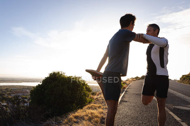 Vista laterale del padre e del figlio caucasico che fanno esercizio di stretching su strada al mattino — Foto stock