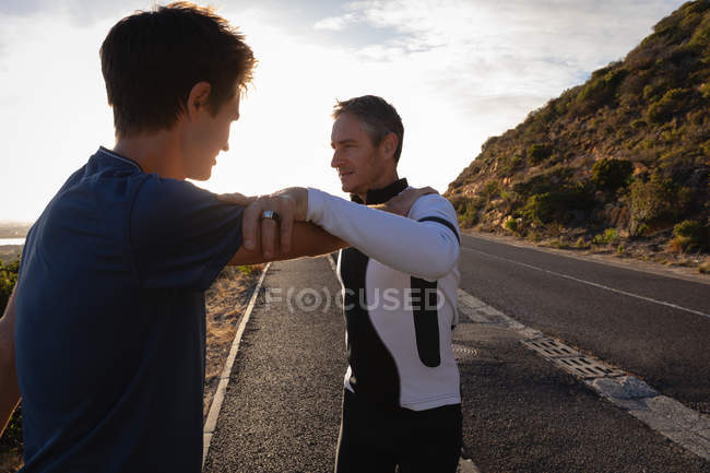 Вид сбоку на отца и сына кавказца, делающего упражнения на растяжку на дороге утром — стоковое фото