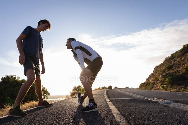 Low angle view of Caucasian father and son doing stretching exercise on road in the morning — Stock Photo